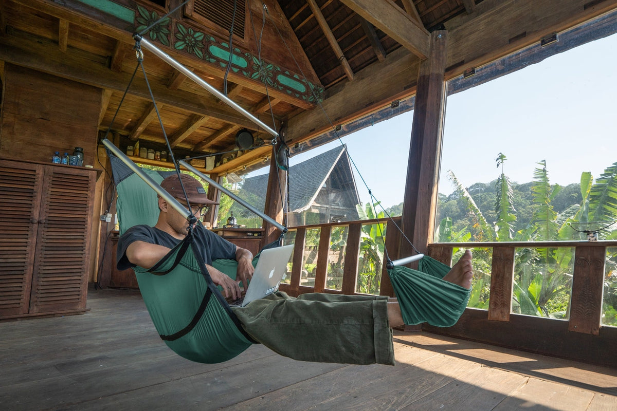 Person with a laptop relaxing in a green Moon Chair, feet in the footrest, on an open veranda with jungle views