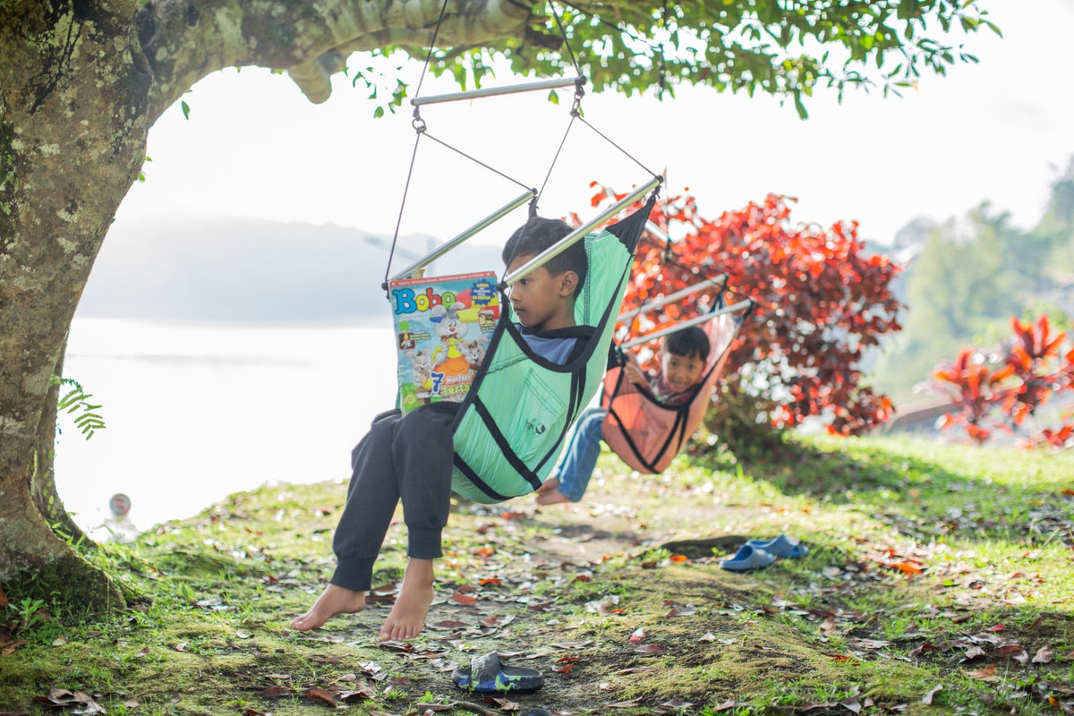 Mini Moon Chair: two children swinging in mint and coral chairs hung from a tree by a lake