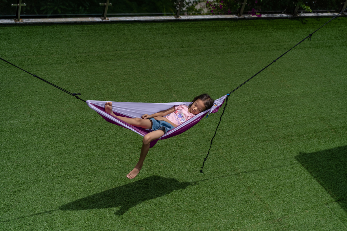 Girl relaxing in a purple Travel Hammock Mini hung low above a lawn