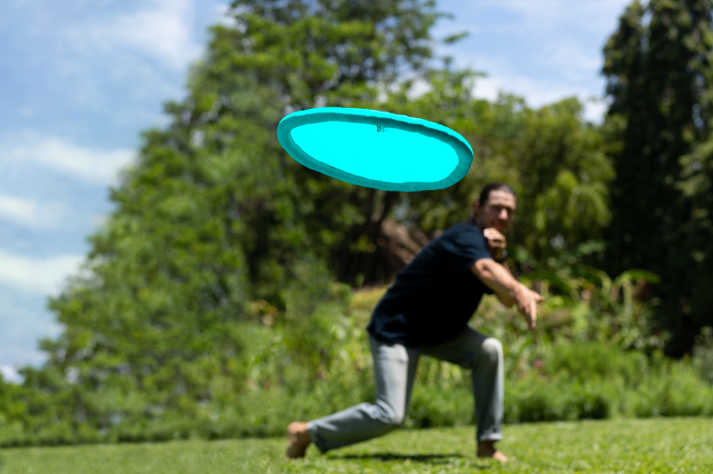 Man throwing a turquoise Moon Disc (Pocket) across a garden lawn