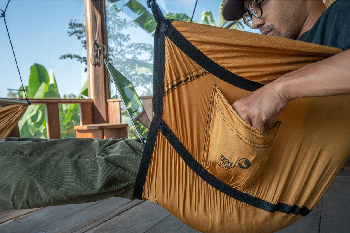Close-up of a person in a mustard Moon Chair reaching into the side pocket, legs stretched out
