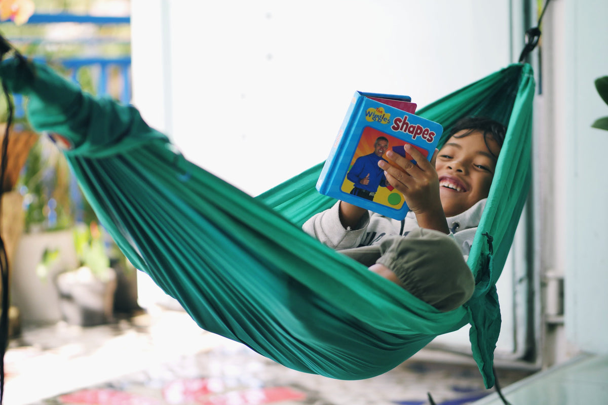 Travel Hammock Mini in green with a smiling child lying inside reading a picture book