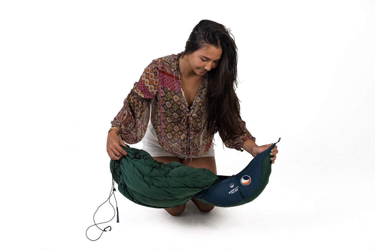 Moonquilt Pro 650 in green held up by a kneeling person, showing its navy stuff sack and drawcord