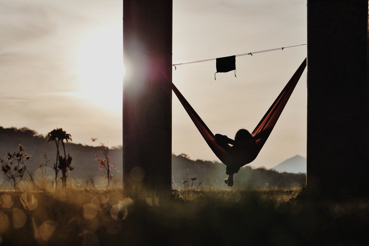 Silhouette of a person in a hammock at sunset, with a Ridgeline strung above holding a pouch