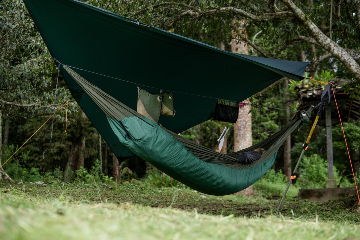 Moon Tarp pitched over a green hammock with underquilt, held out by a trekking pole in a forest camp