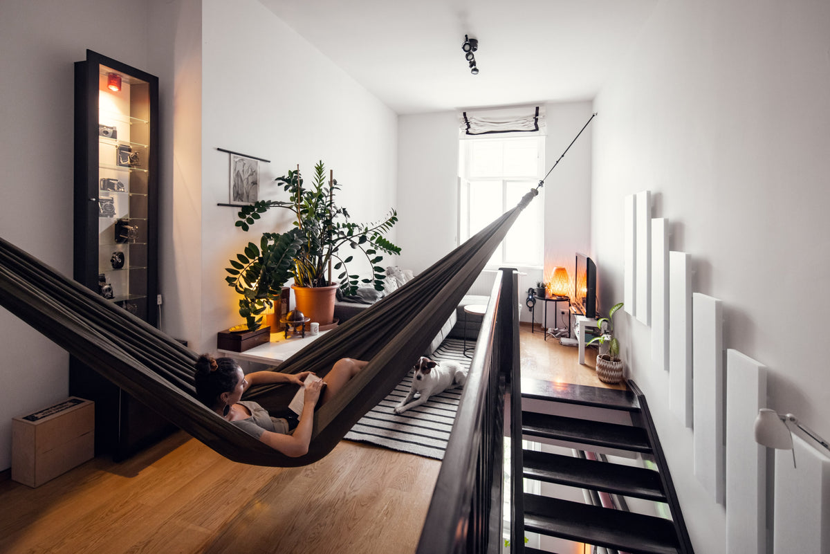 Woman reading in an Olive Brown Home Hammock 420 strung across a bright flat, with a dog lying below