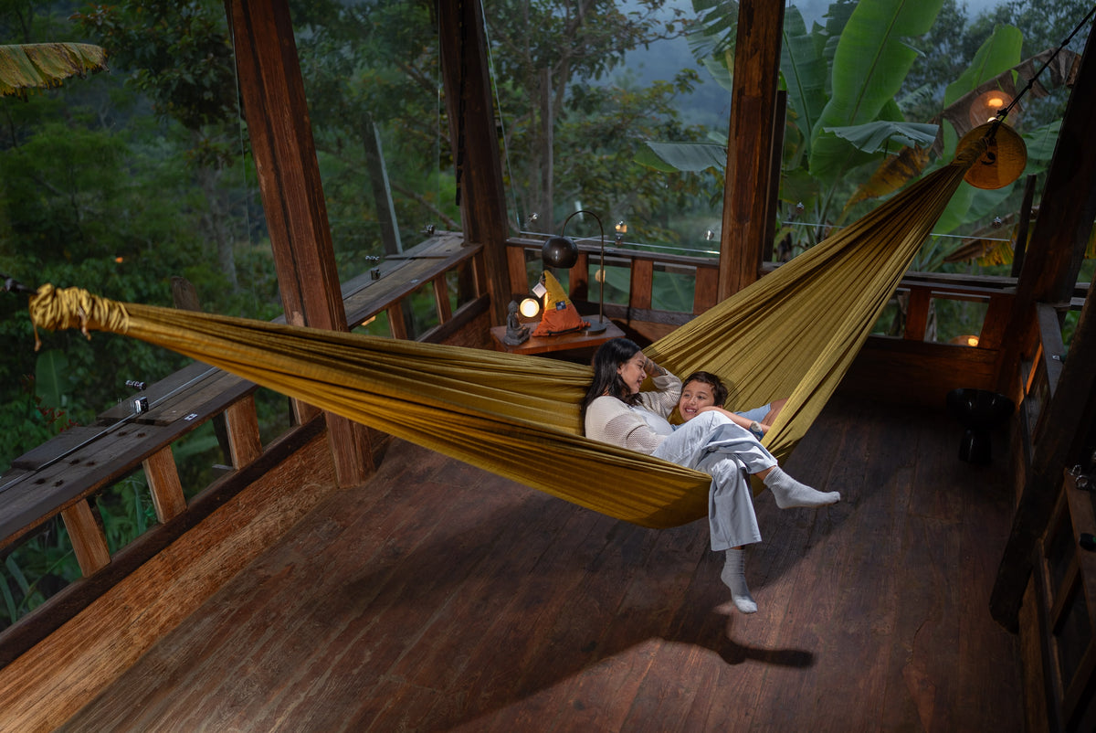Mother and child relaxing in a golden Home Hammock 420 on a wooden deck surrounded by jungle