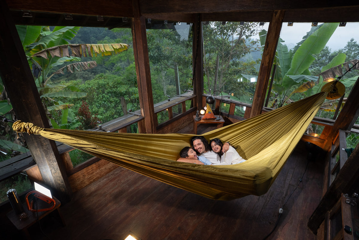 Family of three lying side by side in a golden Home Hammock 520 in an open wooden pavilion