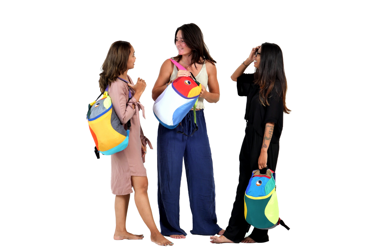 Three women chatting, each with a one-of-a-kind multicoloured Mini Backpack 15L worn or carried