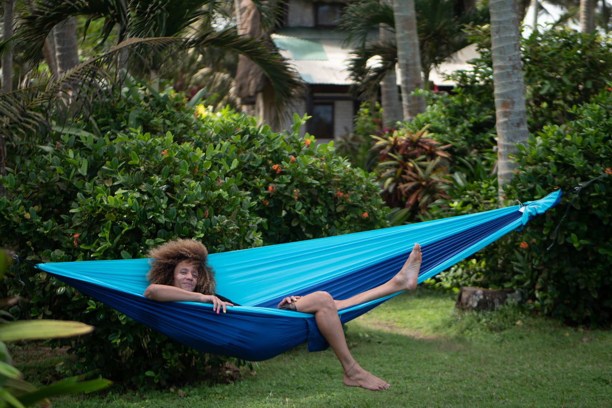 Person relaxing in a Travel Hammock King Size in turquoise and royal blue, hung in a tropical garden