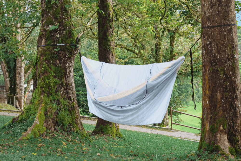 Grey Universal Bug Net 360° zipped around a hammock between mossy trees, front view