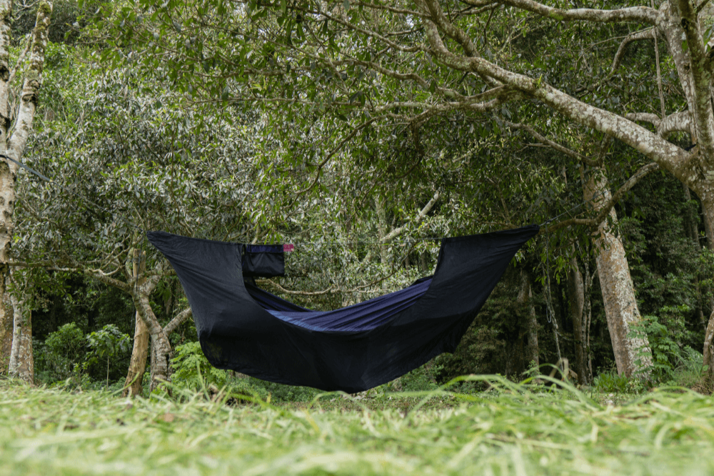 Black Universal Bug Net 360° enclosing a hammock hung between trees in a forest clearing