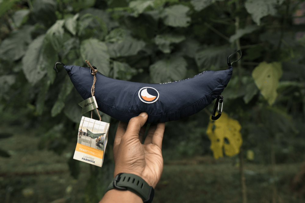 Hand holding the navy Lightest Hammock packed in its compact stuff sack, with carabiners and product tag