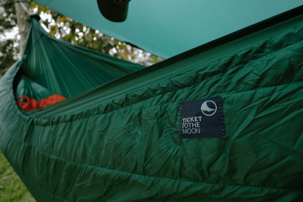 Green Moonquilt Pro 650 wrapped beneath a hammock under a tarp, close-up of its Ticket To The Moon label