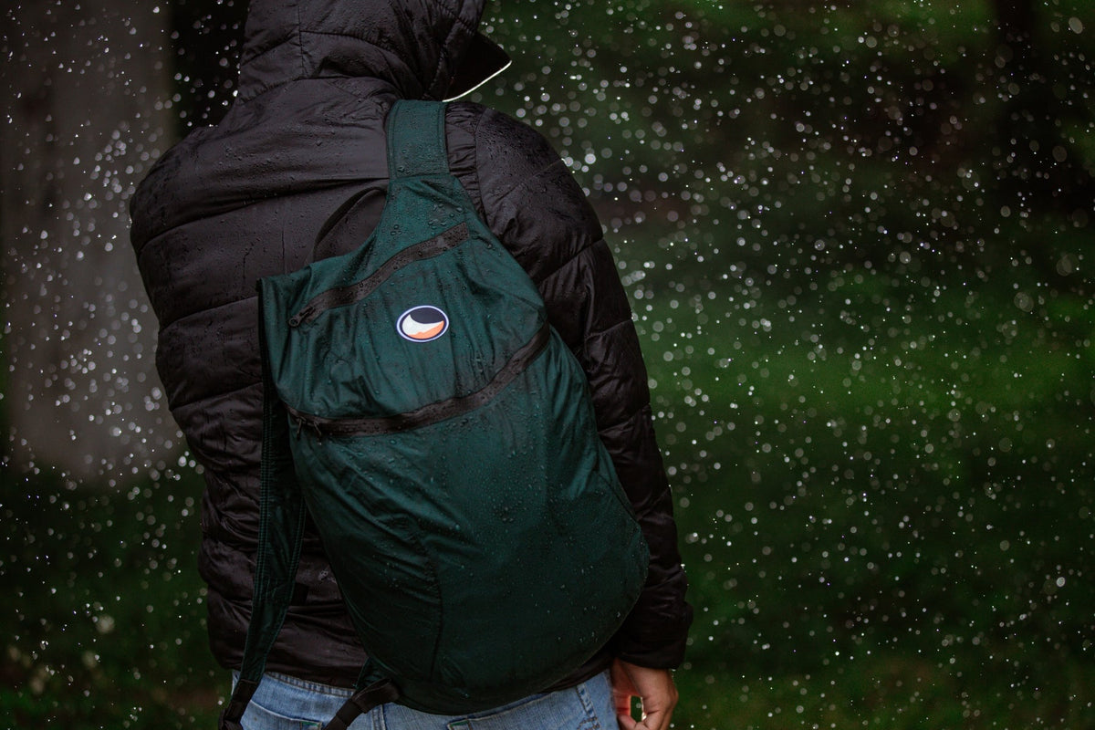 Person in a black puffer jacket wearing a dark green Backpack Plus 25L (Water Resistant) in falling rain