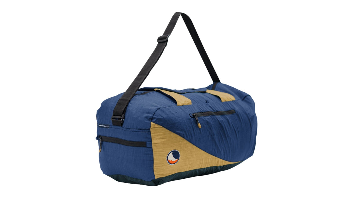 Moon Carrier in blue and gold, a duffel bag with black shoulder strap and side zip pockets