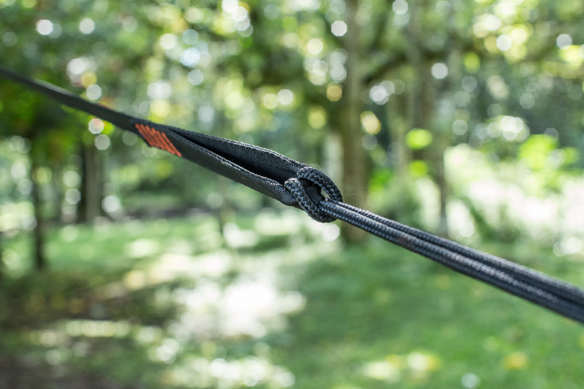 Close-up of Tree Friendly Extender (2-Pack) looped onto a black hammock strap with a forest in the background