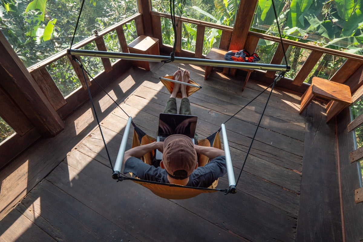 Overhead view of a person working on a laptop in an orange Moon Chair on a wooden treehouse deck