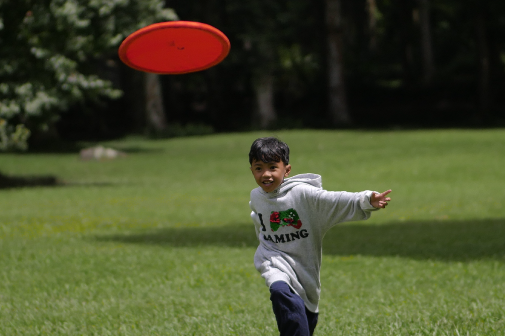 Boy running on a lawn after throwing a red Moon Disc (Pocket)