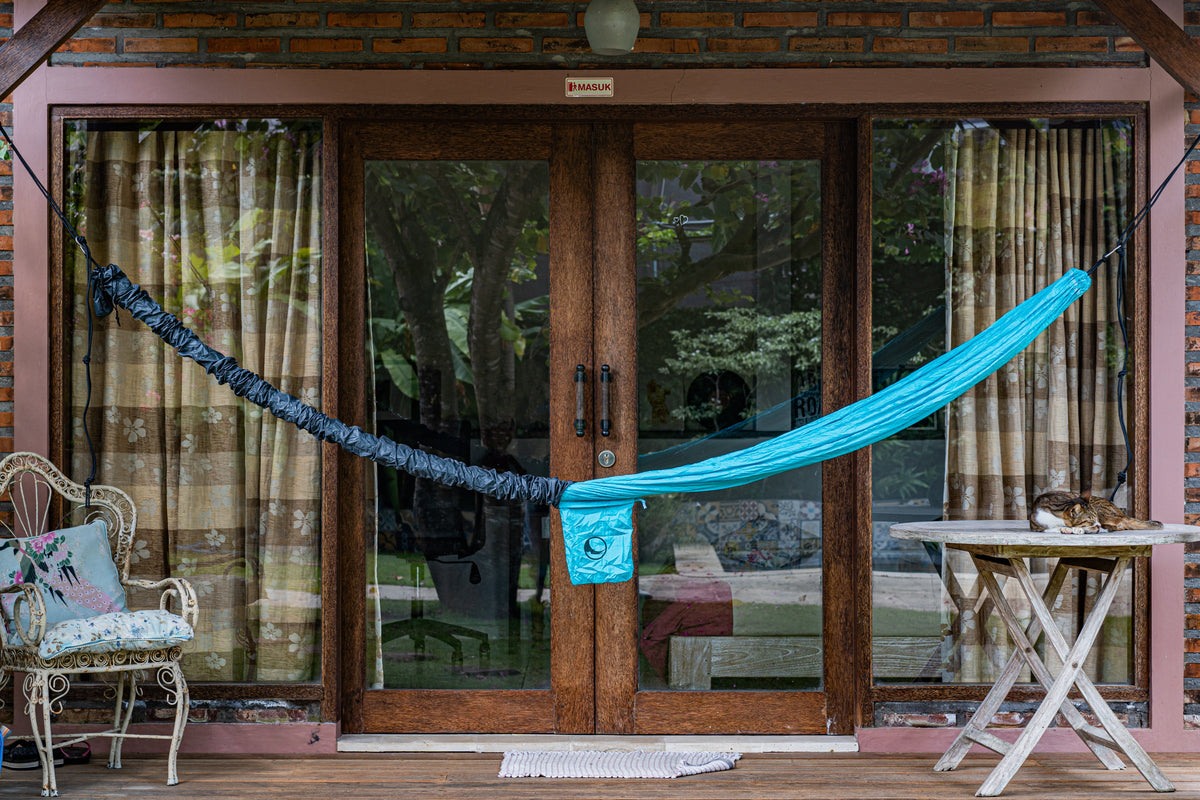 UV-Proof Hammock Sleeve in navy covering one half of a turquoise hammock hung across a porch's glass doors