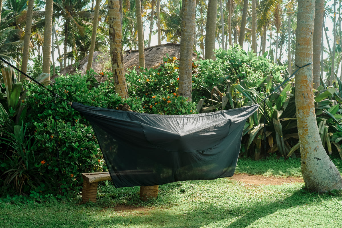 Universal Bug Net 360° in dark green hanging between palm trees in a tropical garden