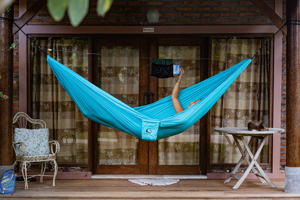 Ridgeline strung above a turquoise hammock on a porch, holding a hanging pouch while a hand reaches for a cup