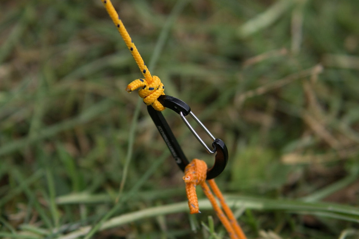 Close-up of a yellow Moon Tarp guyline tied to a black mini carabiner on grass