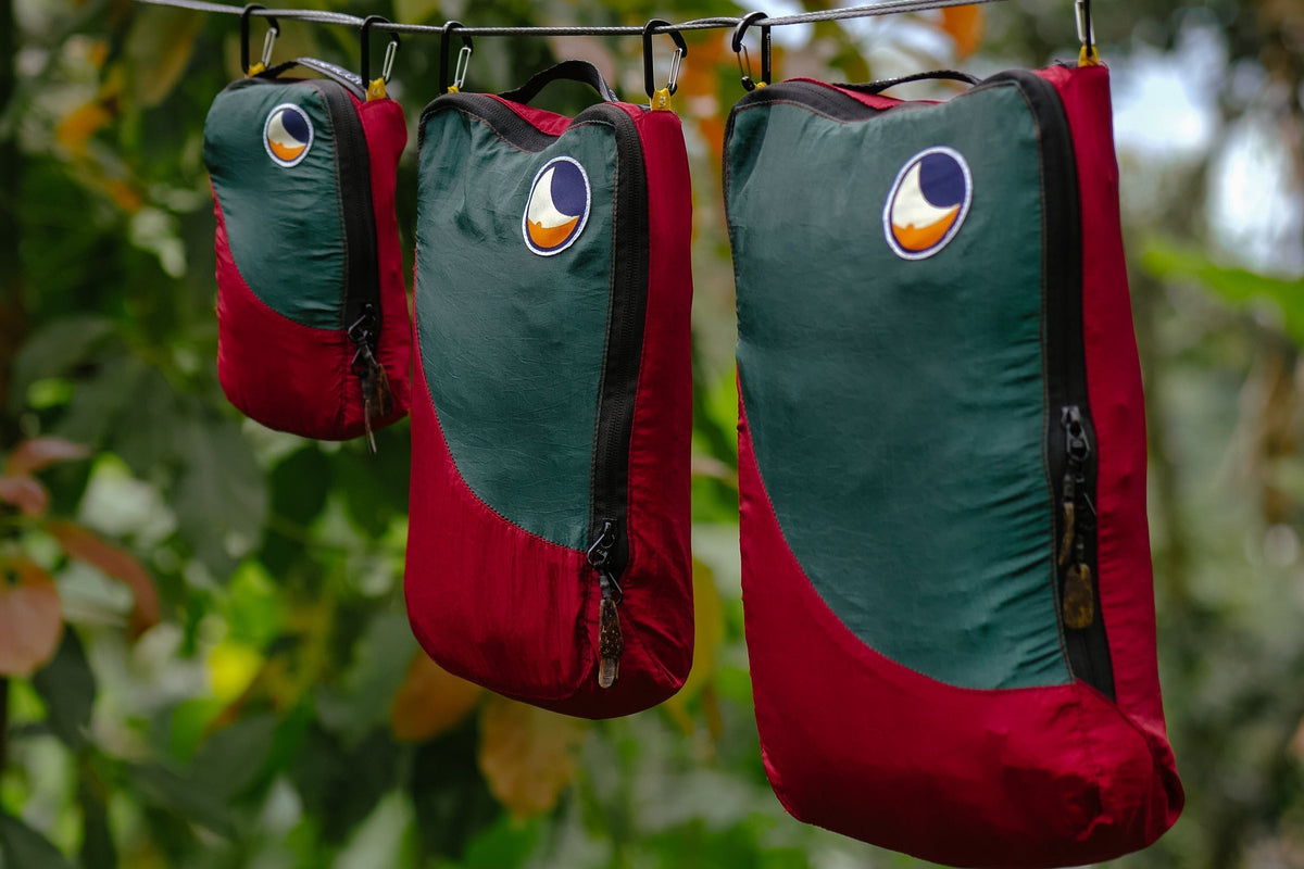 Travel Cube Set in green and red: small, medium and large packing cubes hanging from a line with carabiners