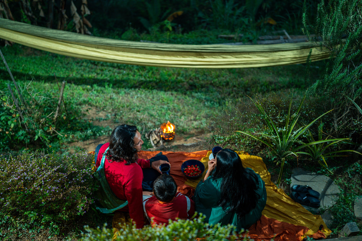 Family sitting by a small campfire on a picnic blanket under a golden Home Hammock 520 at dusk