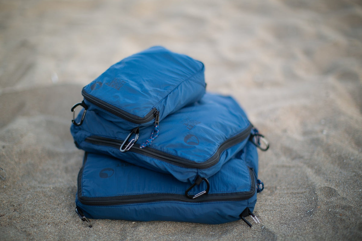 Travel Cube Set in blue: three packing cubes stacked on sand