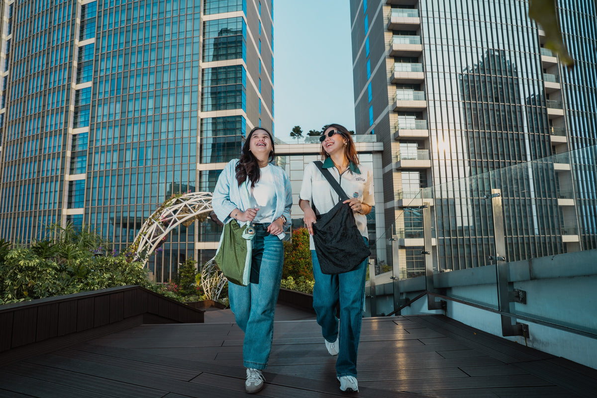 Two friends laughing as they walk across a rooftop deck carrying Leaf Green and Black Moon Bag Medium bags