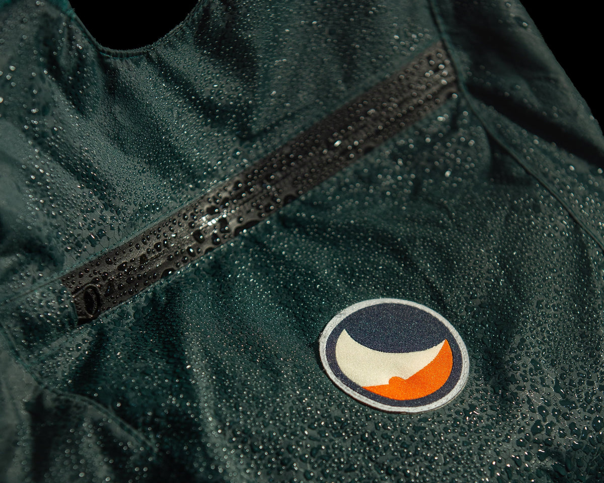 Raindrops beading on the green Backpack Plus 25L Water Resistant around the front zip pocket and moon logo patch
