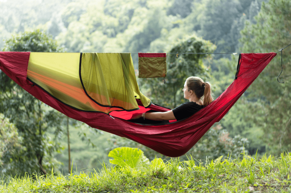 Person sitting in a red Pro Hammock (Custom) with its bug net pulled back, a hanging pouch on the ridgeline